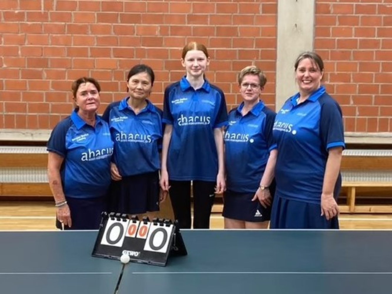 Fünf Mitglieder der TTCE-Damenmannschaft hinter einem Tischtennis-Tisch mit Zähltafel