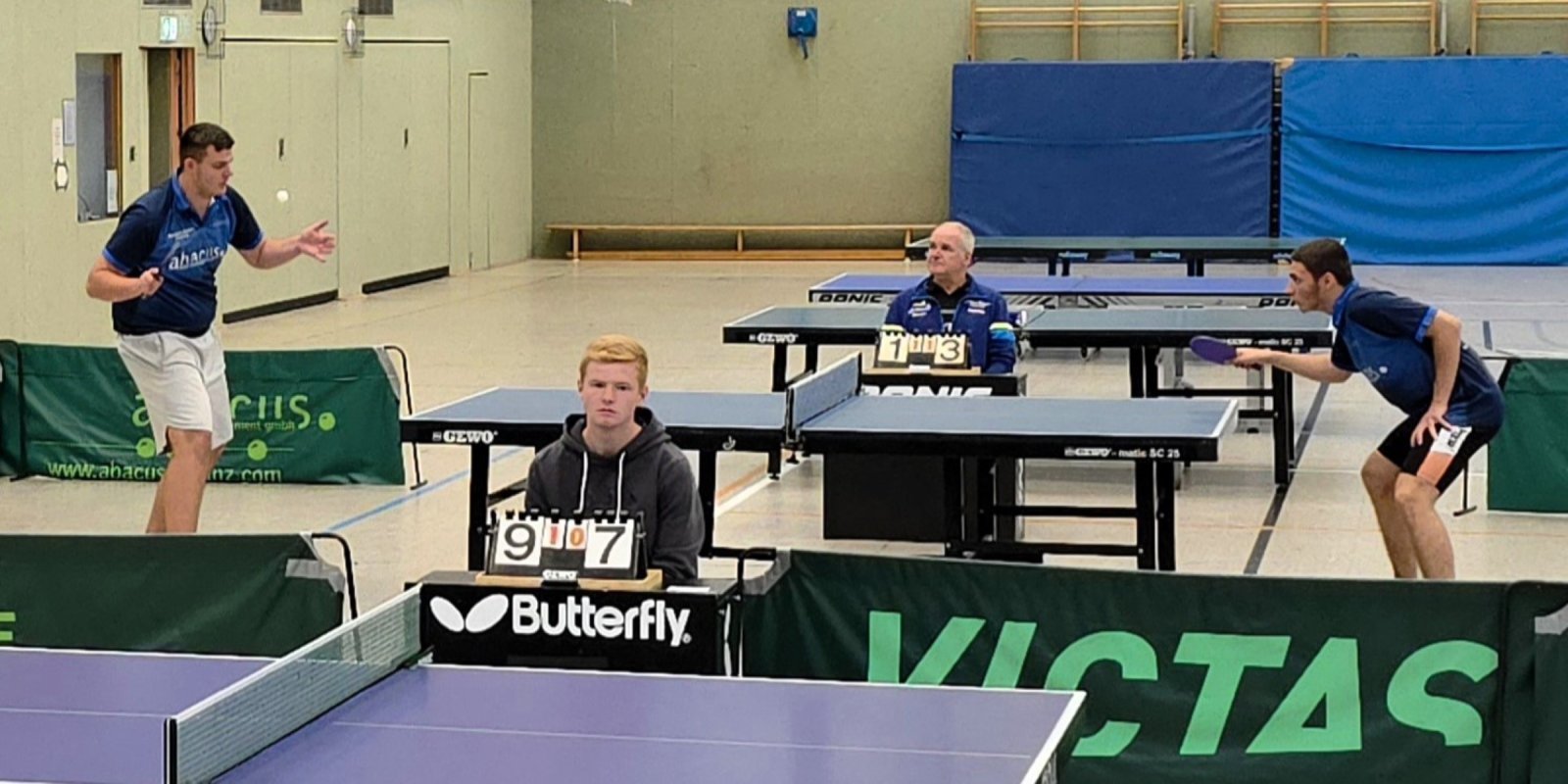 Ein Tischtennis-Einzel zwischen zwei Jugendlichen mit Punktestand 1:3 bei 1:1 Sätzen - im Vordergrund eine weitere Zähltafel mit Punktestand 9:7 bei 1:0 Sätzen