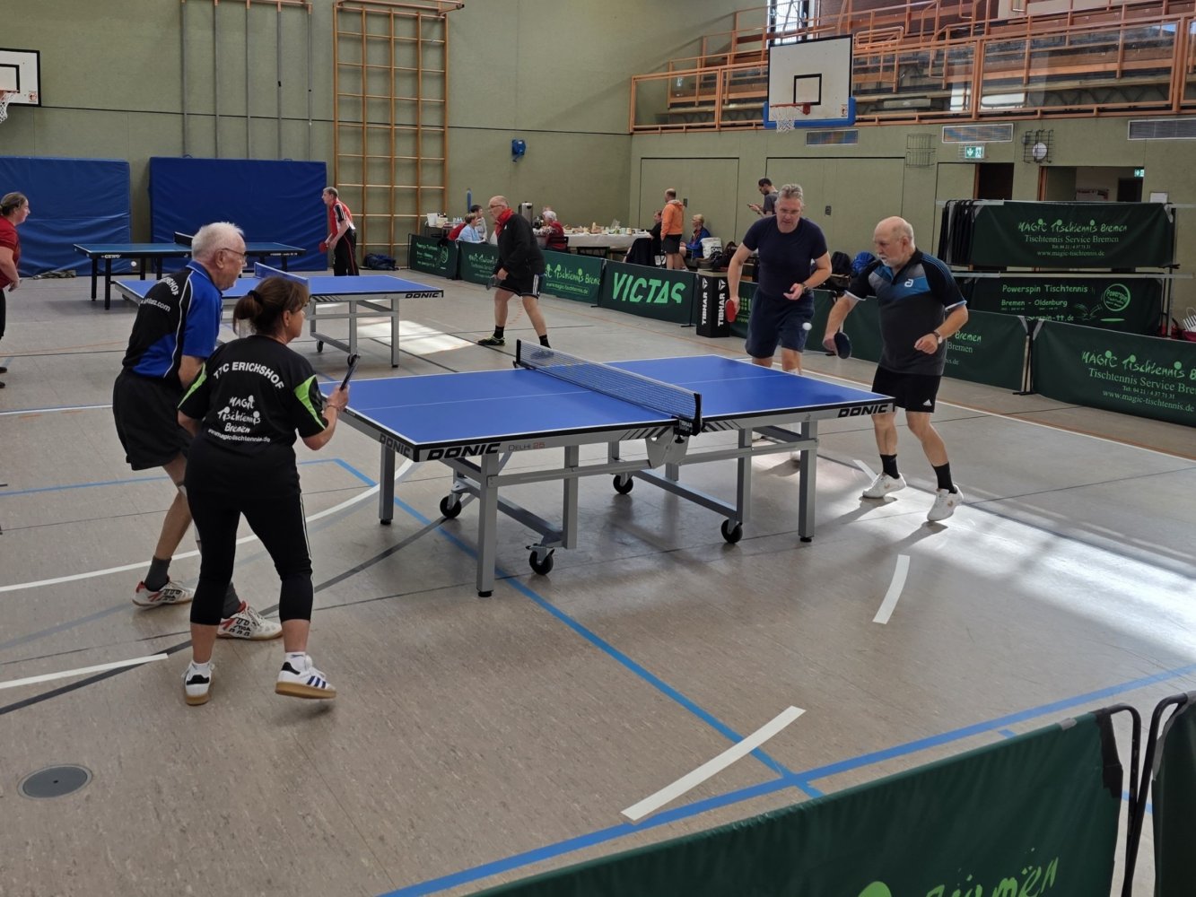 Tischtennis-Doppel an einem Tisch mit weiteren Partien im Hintergrund